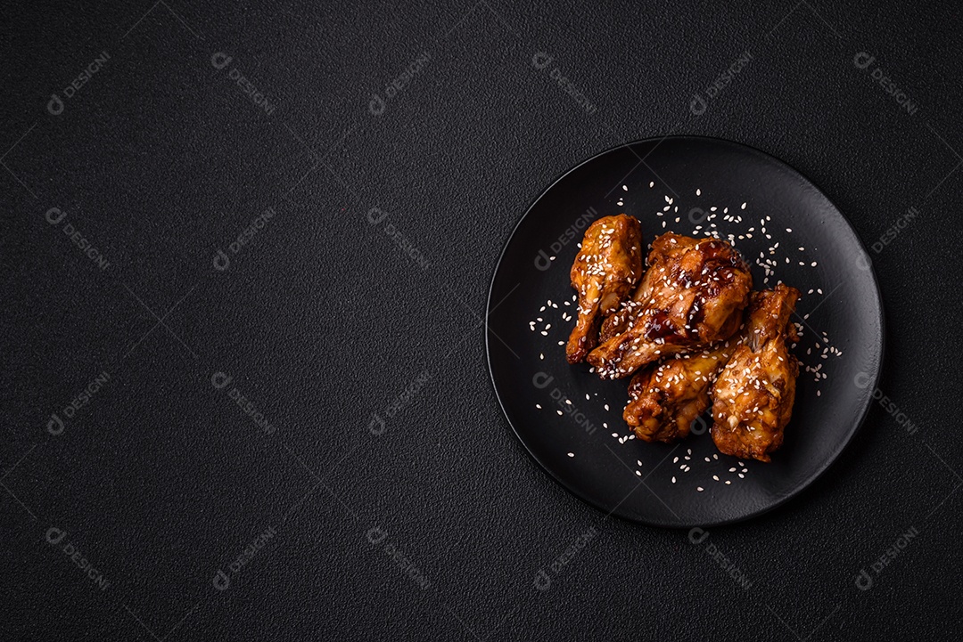 Deliciosas asas grelhadas crocantes com molho teriyaki com sal, especiarias e ervas sobre um fundo escuro de concreto
