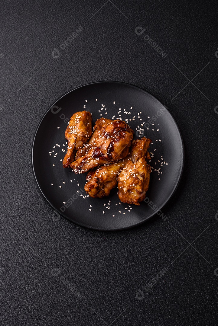 Deliciosas asas grelhadas crocantes com molho teriyaki com sal, especiarias e ervas sobre um fundo escuro de concreto