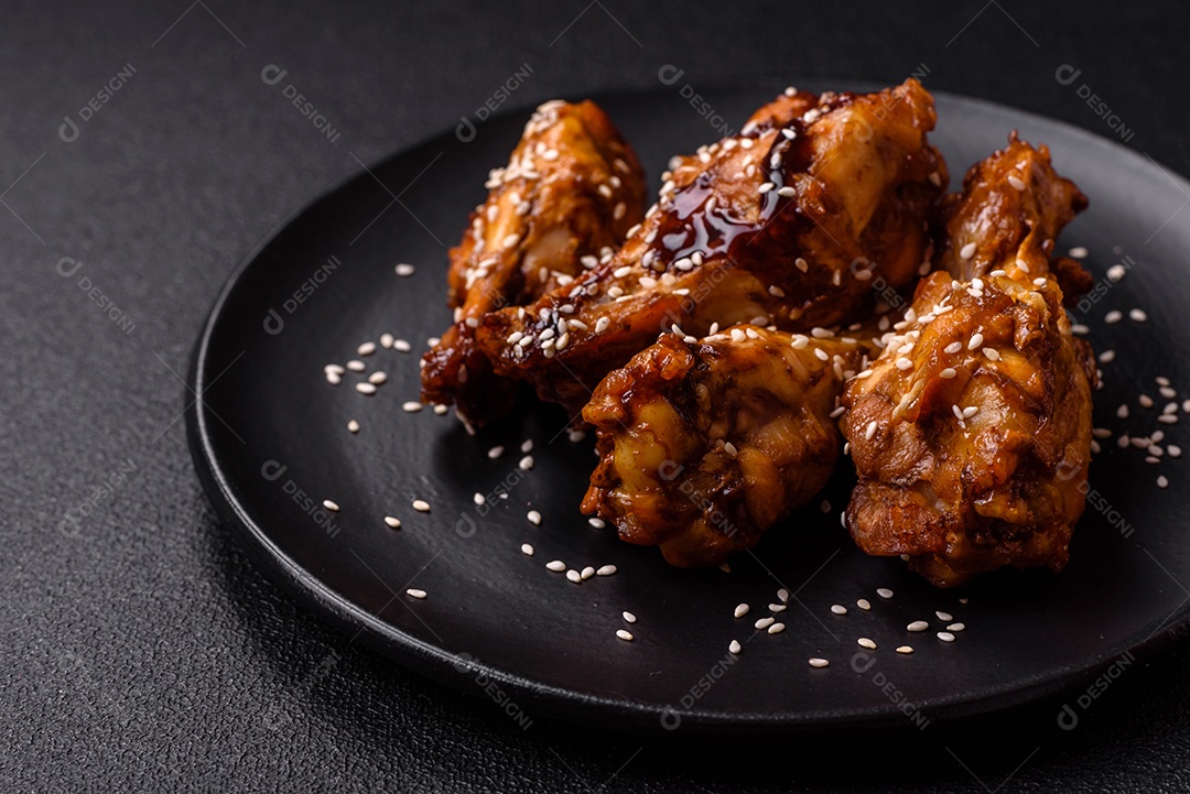 Deliciosas asas grelhadas crocantes com molho teriyaki com sal, especiarias e ervas sobre um fundo escuro de concreto