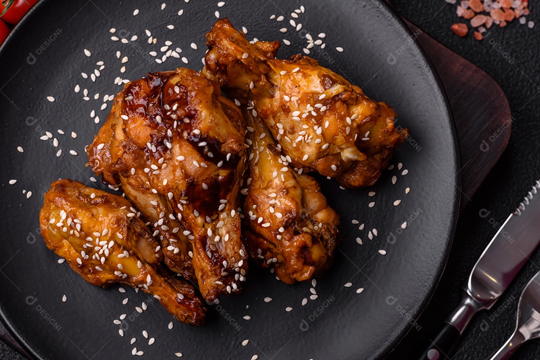 Deliciosas asas grelhadas crocantes com molho teriyaki com sal, especiarias e ervas sobre um fundo escuro de concreto
