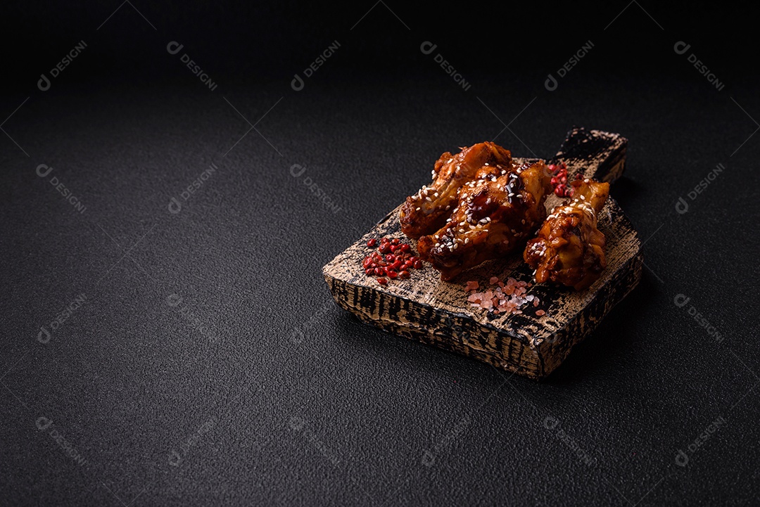 Deliciosas asas grelhadas crocantes com molho teriyaki com sal, especiarias e ervas sobre um fundo escuro de concreto