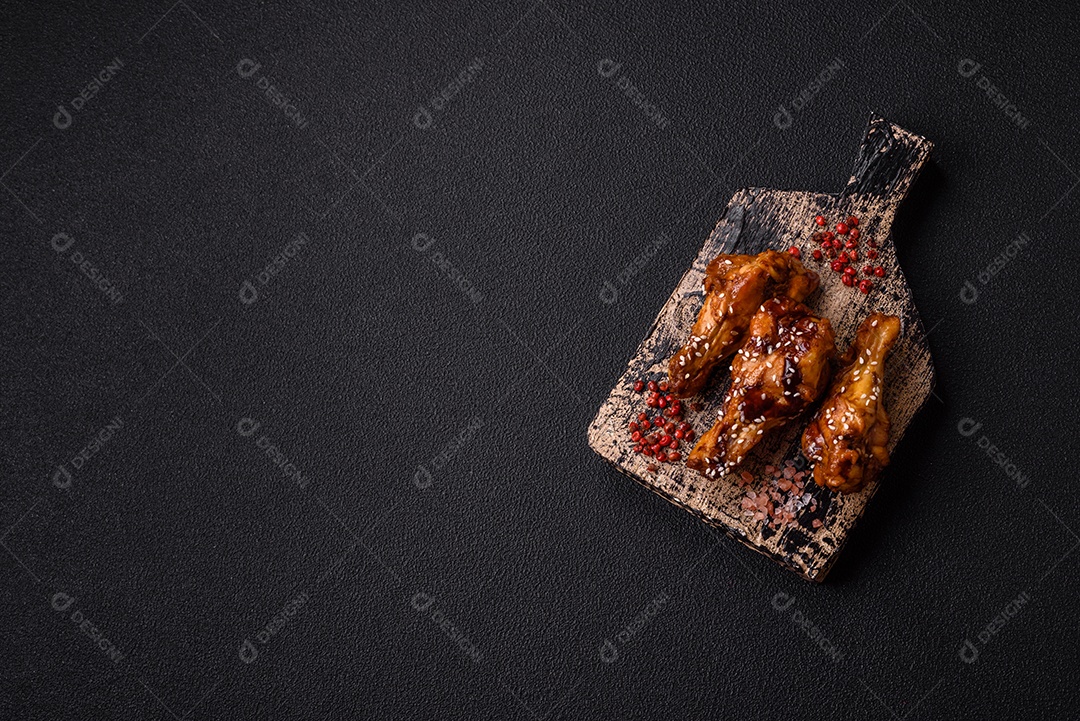 Deliciosas asas grelhadas crocantes com molho teriyaki com sal, especiarias e ervas sobre um fundo escuro de concreto