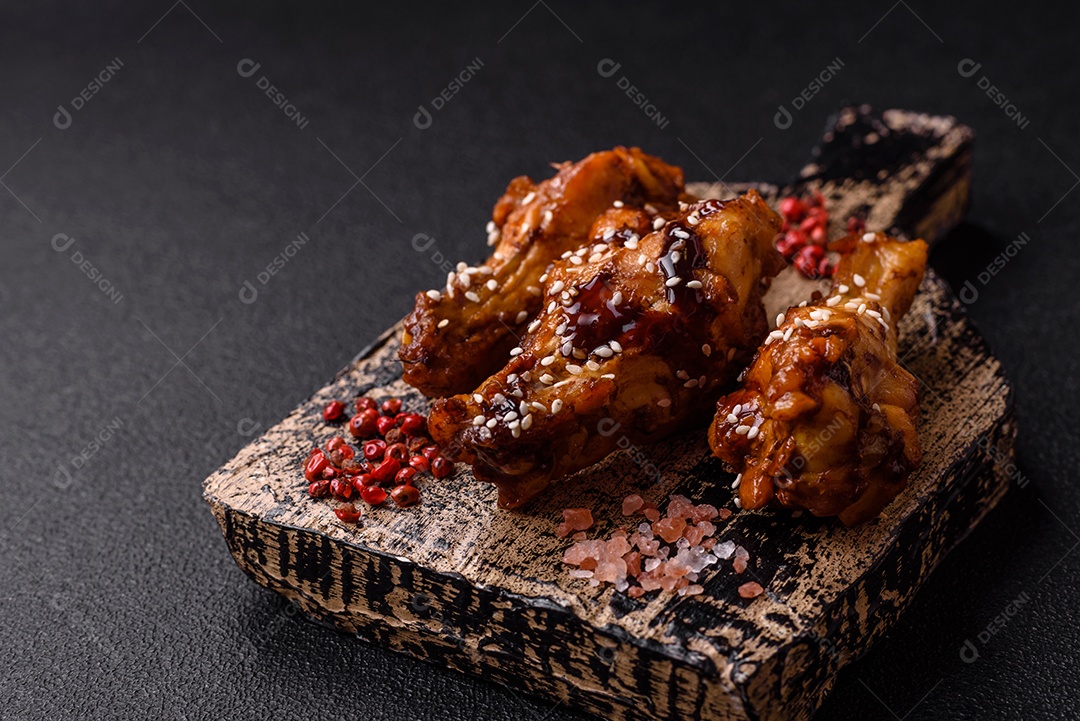 Deliciosas asas grelhadas crocantes com molho teriyaki com sal, especiarias e ervas sobre um fundo escuro de concreto