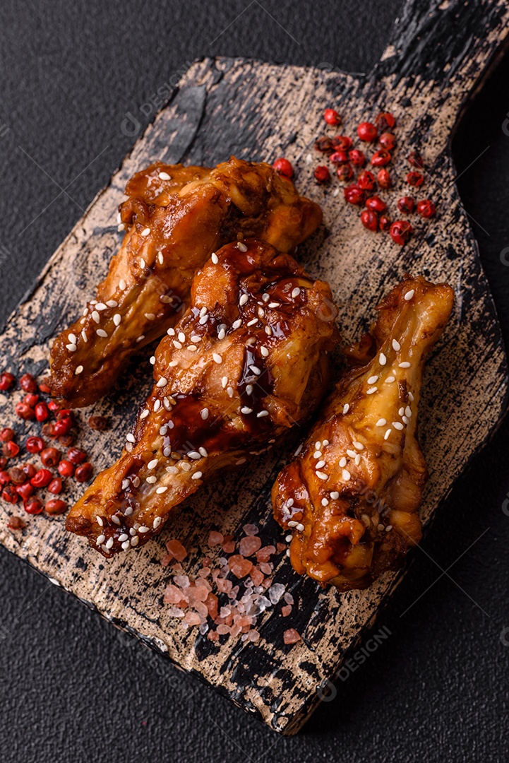 Deliciosas asas grelhadas crocantes com molho teriyaki com sal, especiarias e ervas sobre um fundo escuro de concreto