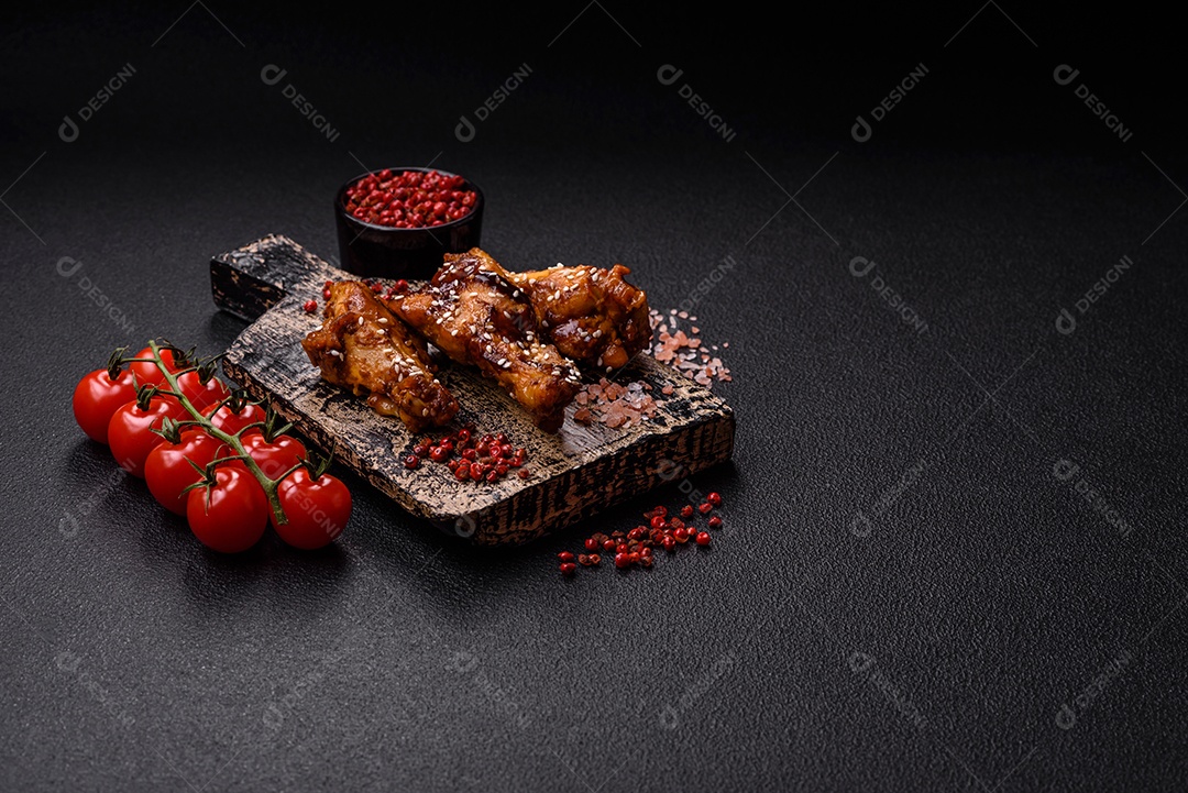 Deliciosas asas grelhadas crocantes com molho teriyaki com sal, especiarias e ervas sobre um fundo escuro de concreto