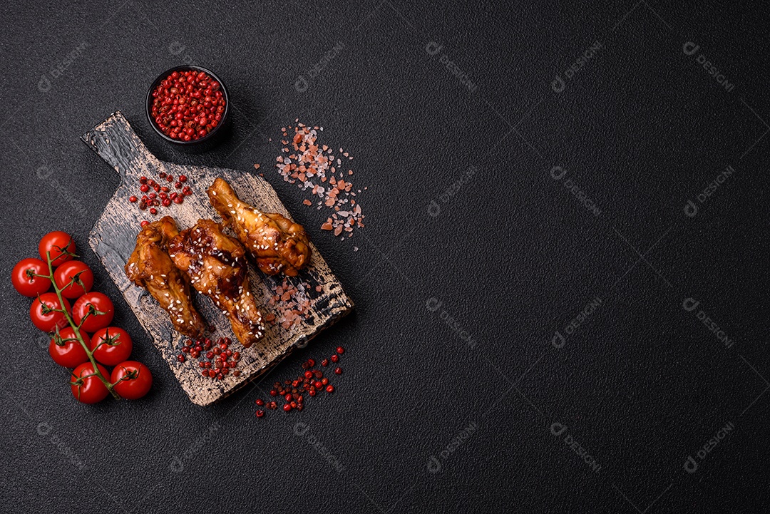 Deliciosas asas grelhadas crocantes com molho teriyaki com sal, especiarias e ervas sobre um fundo escuro de concreto