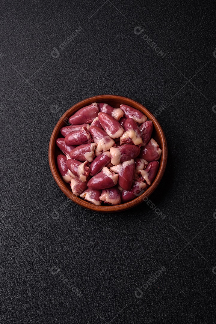 Corações de frango cru com sal, especiarias e ervas sobre um fundo escuro de concreto