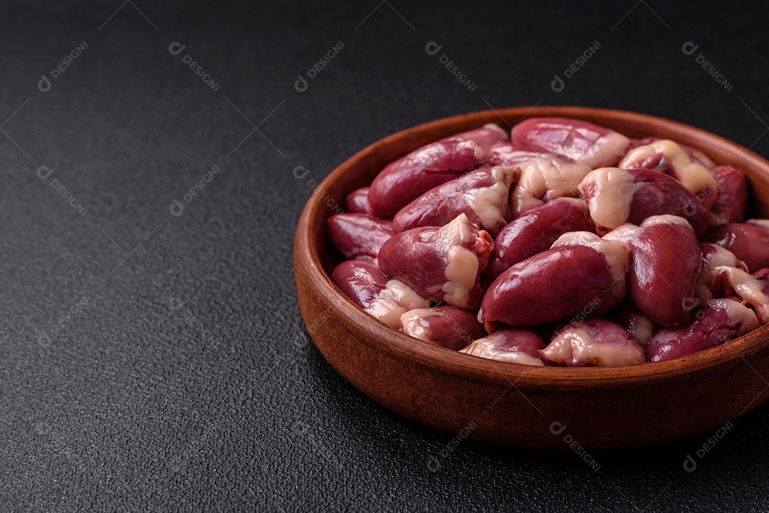 Corações de frango cru com sal, especiarias e ervas sobre um fundo escuro de concreto