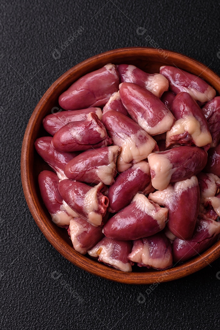 Corações de frango cru com sal, especiarias e ervas sobre um fundo escuro de concreto