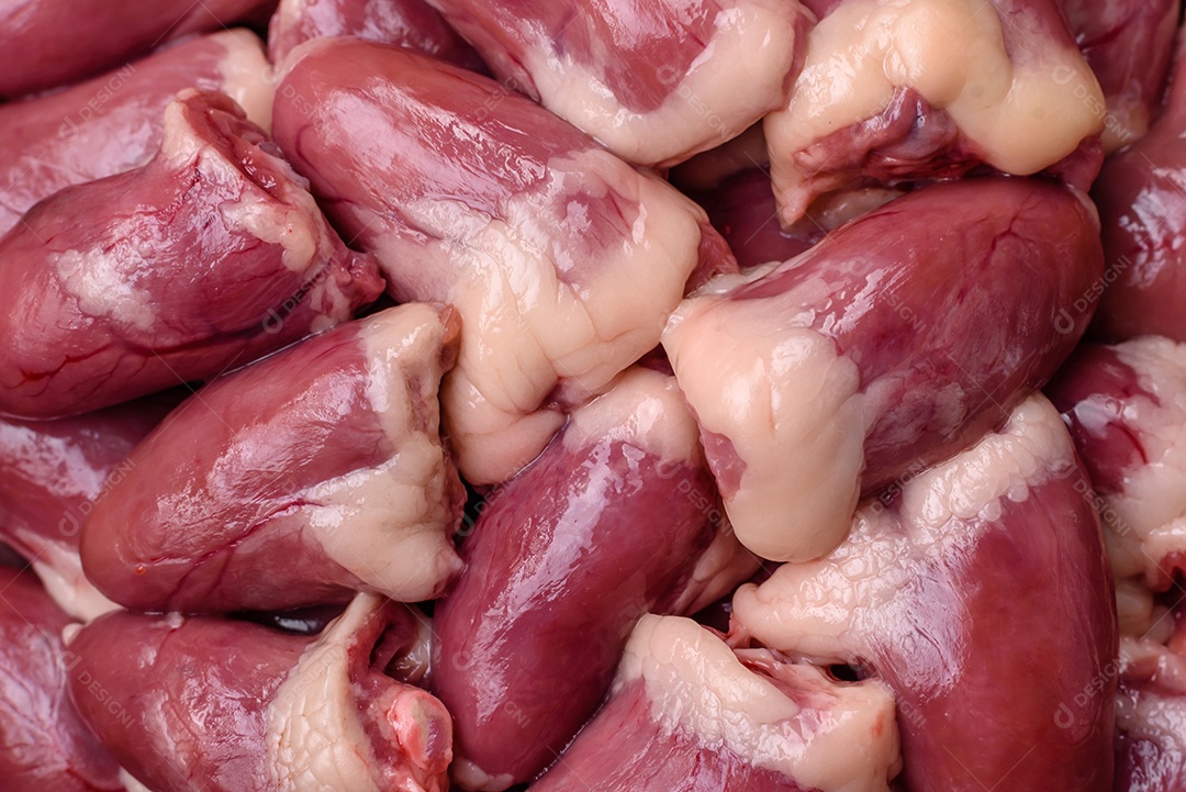 Corações de frango cru com sal, especiarias e ervas sobre um fundo escuro de concreto