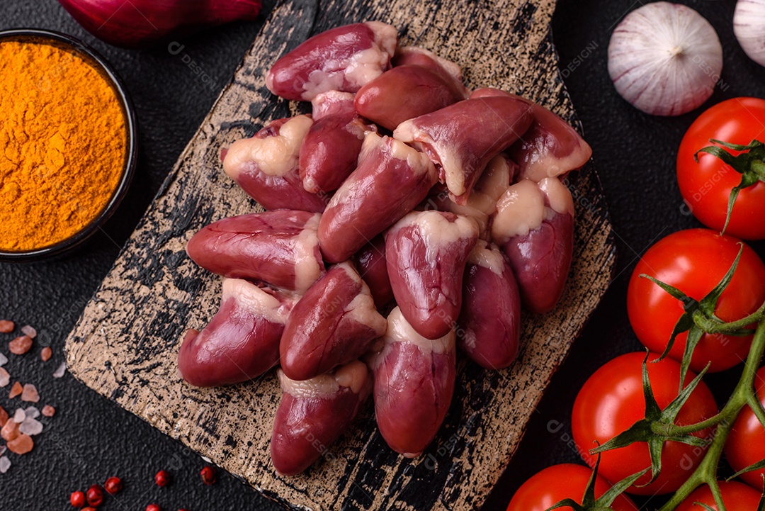 Corações de frango cru com sal, especiarias e ervas sobre um fundo escuro de concreto