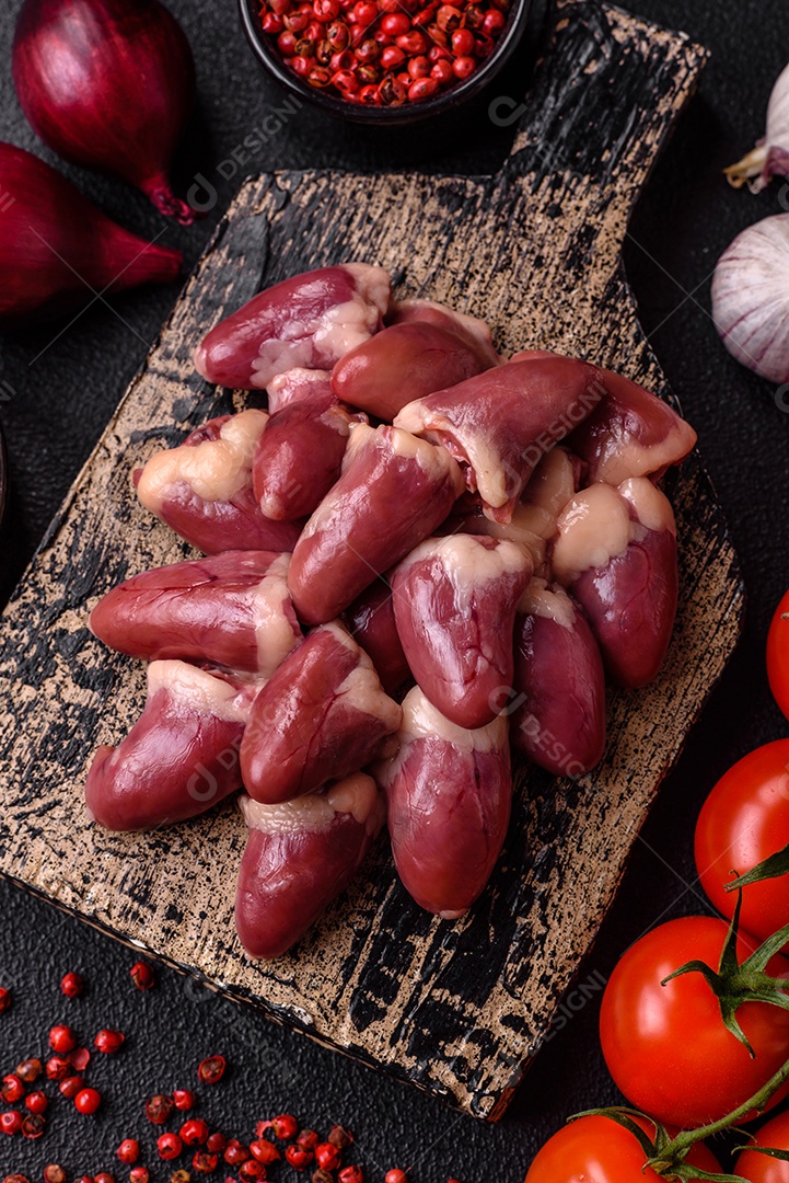 Corações de frango cru com sal, especiarias e ervas sobre um fundo escuro de concreto