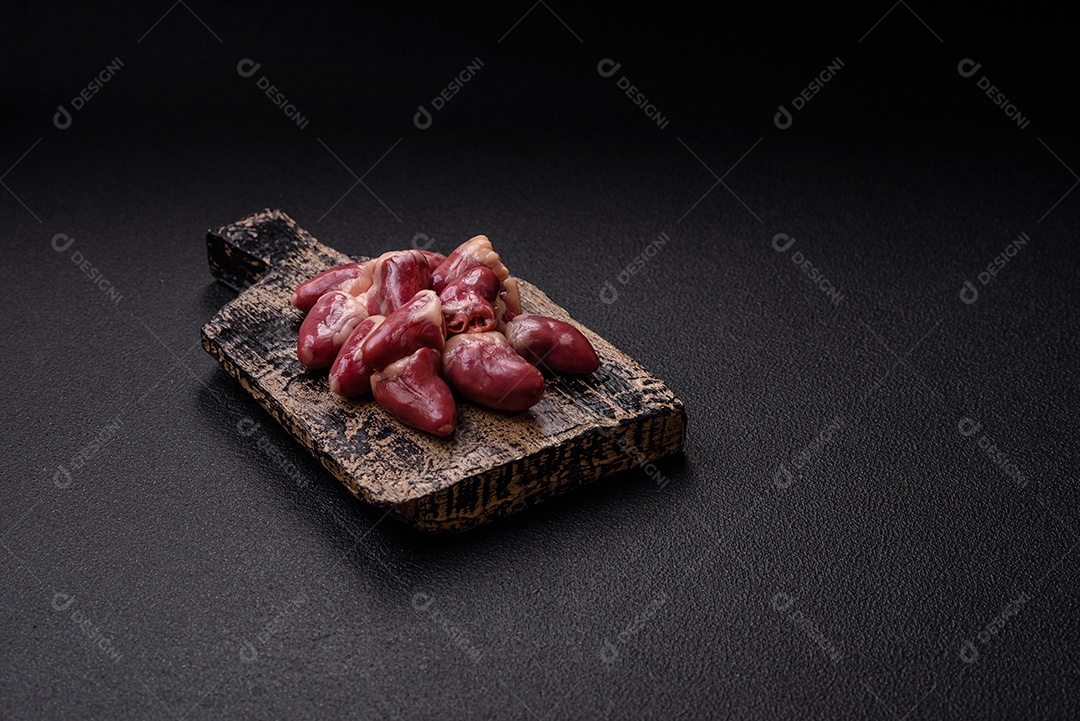 Corações de frango cru com sal, especiarias e ervas sobre um fundo escuro de concreto