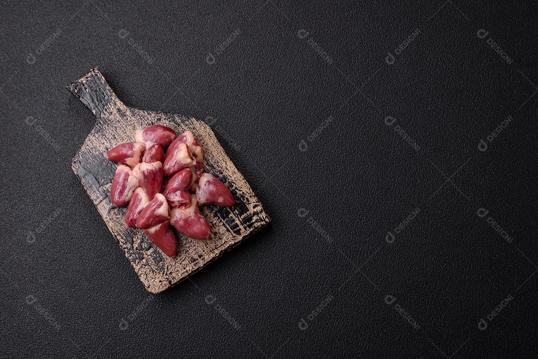 Corações de frango cru com sal, especiarias e ervas sobre um fundo escuro de concreto
