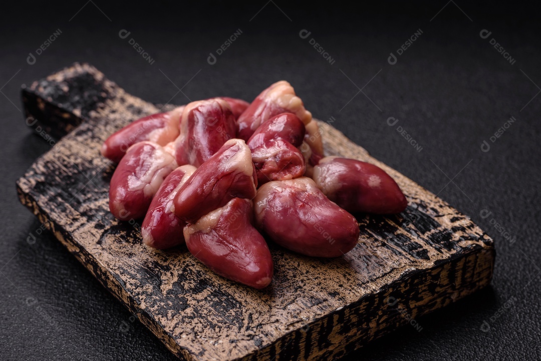 Corações de frango cru com sal, especiarias e ervas sobre um fundo escuro de concreto