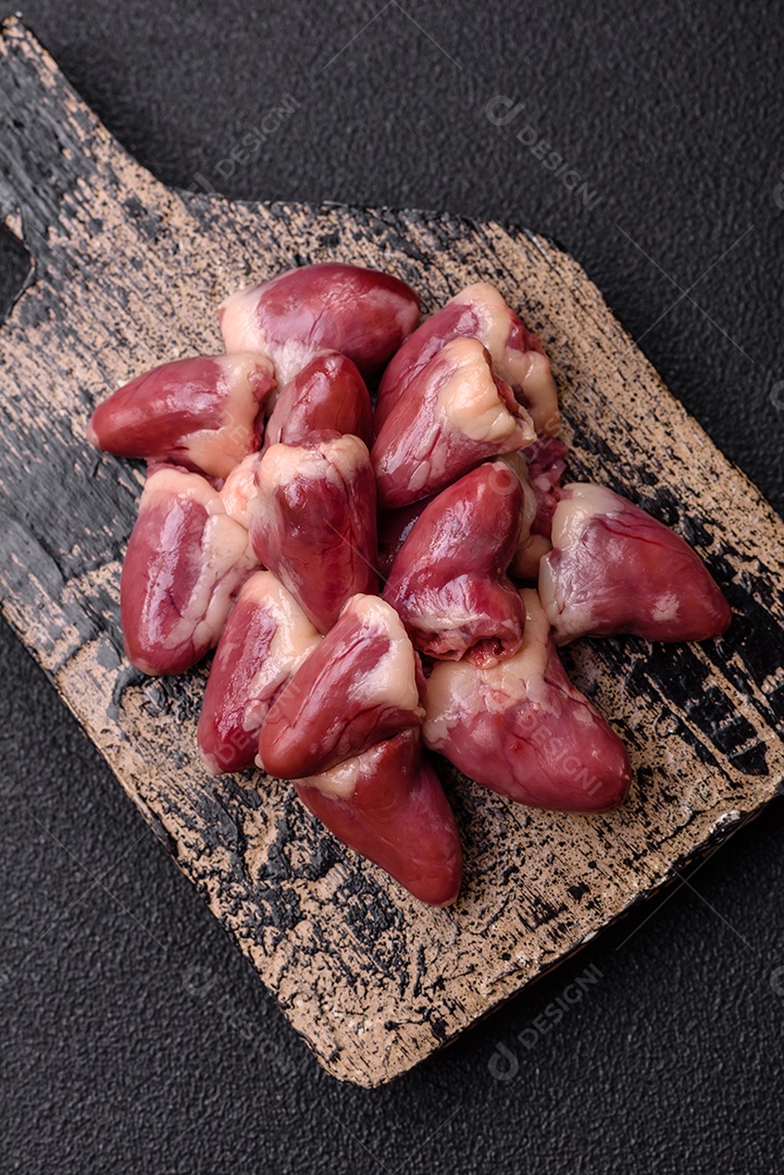 Corações de frango cru com sal, especiarias e ervas sobre um fundo escuro de concreto