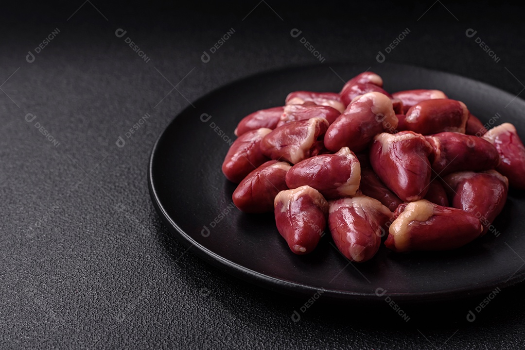 Corações de frango cru com sal, especiarias e ervas sobre um fundo escuro de concreto