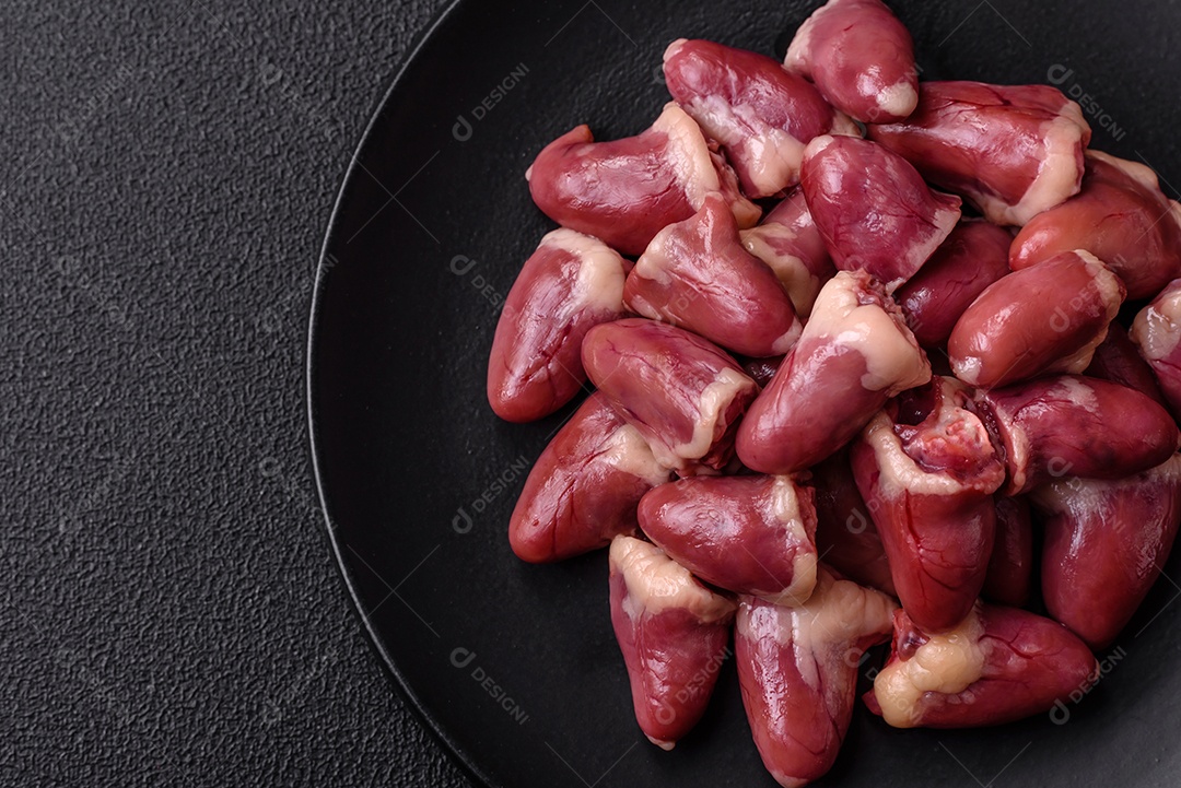 Corações de frango cru com sal, especiarias e ervas sobre um fundo escuro de concreto