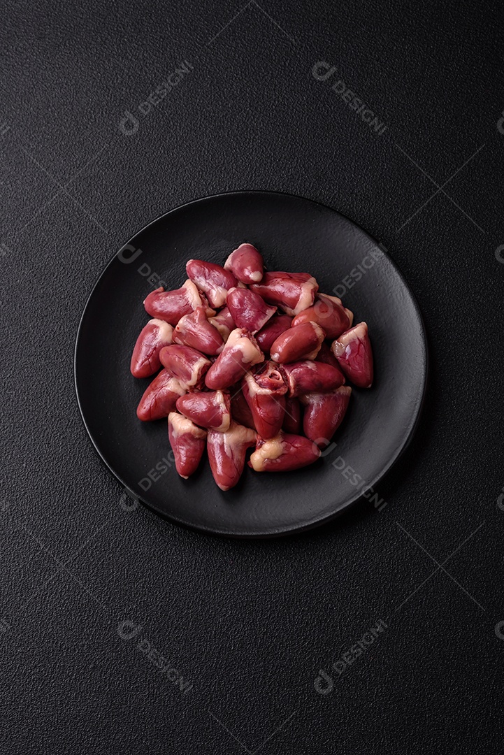 Corações de frango cru com sal, especiarias e ervas sobre um fundo escuro de concreto