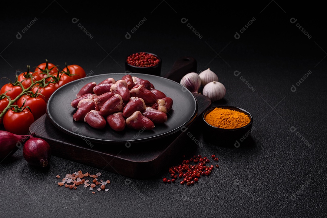 Corações de frango cru com sal, especiarias e ervas sobre um fundo escuro de concret