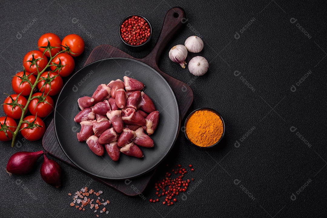 Corações de frango cru com sal, especiarias e ervas sobre um fundo escuro de concreto