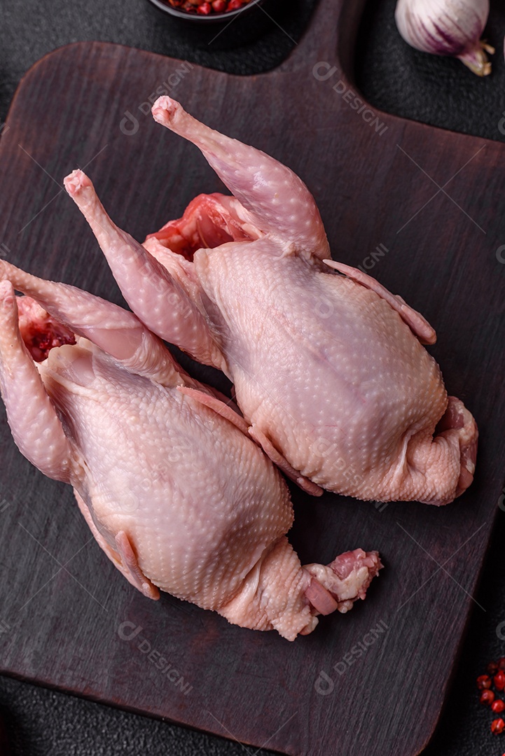 Codornizes cruas inteiras com sal, especiarias e ervas sobre um fundo escuro de concreto preparado para assar