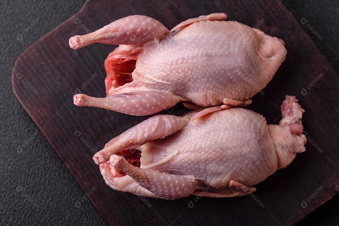 Codornizes cruas inteiras com sal, especiarias e ervas sobre um fundo escuro de concreto preparado para assar