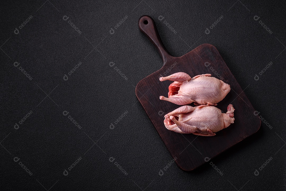 Codornizes cruas inteiras com sal, especiarias e ervas sobre um fundo escuro de concreto preparado para assar