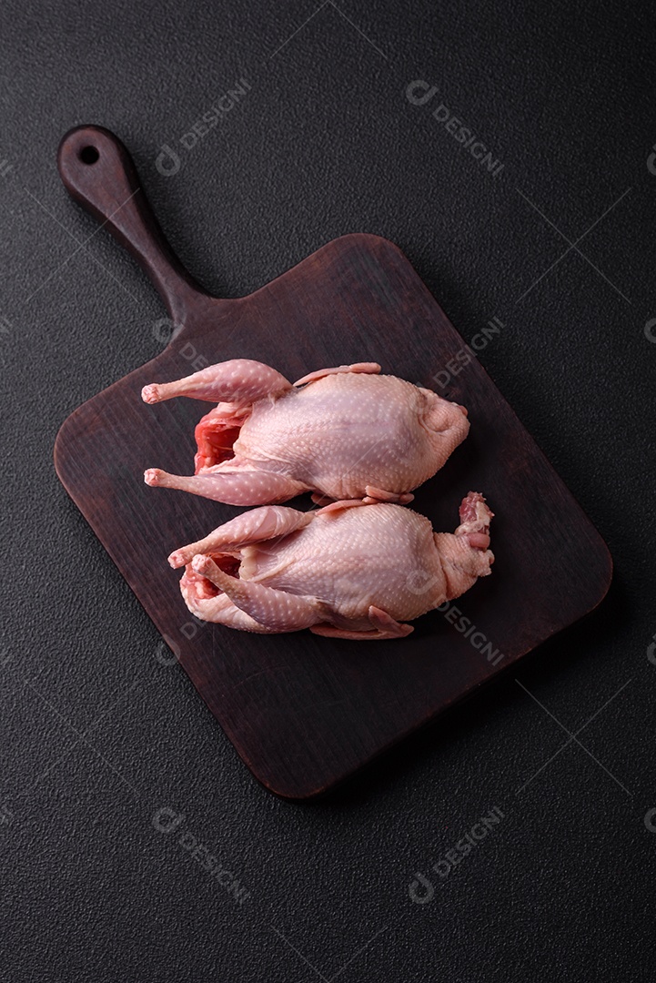 Codornizes cruas inteiras com sal, especiarias e ervas sobre um fundo escuro de concreto preparado para assar