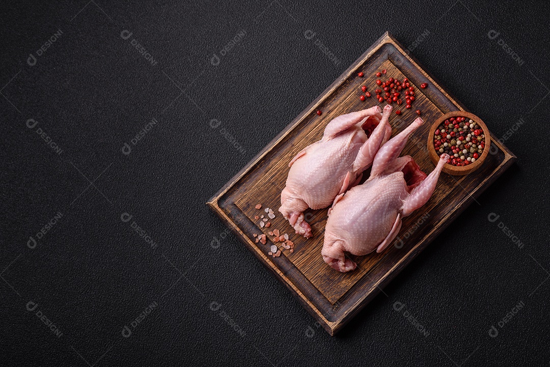 Codornizes cruas inteiras com sal, especiarias e ervas sobre um fundo escuro de concreto preparado para assar