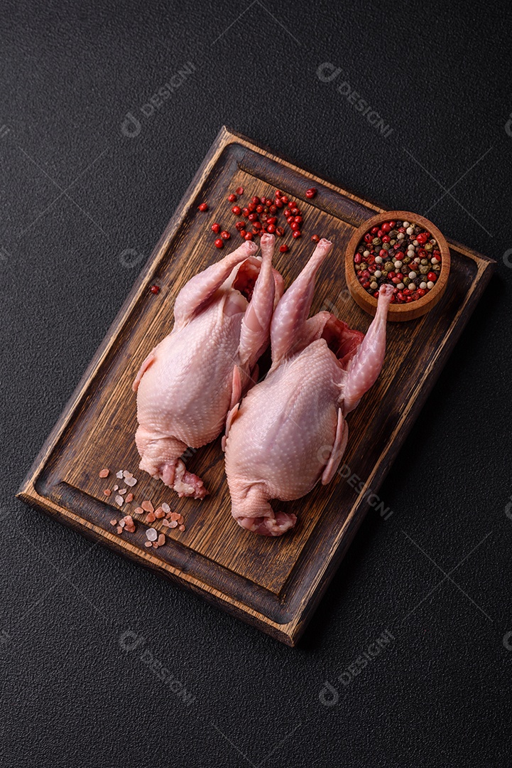 Codornizes cruas inteiras com sal, especiarias e ervas sobre um fundo escuro de concreto preparado para assar