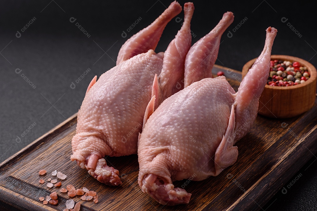 Codornizes cruas inteiras com sal, especiarias e ervas sobre um fundo escuro de concreto preparado para assar