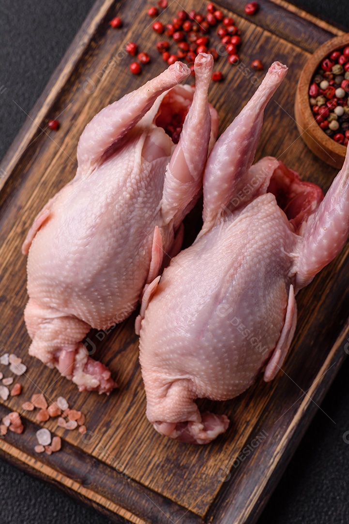 Codornizes cruas inteiras com sal, especiarias e ervas sobre um fundo escuro de concreto preparado para assar