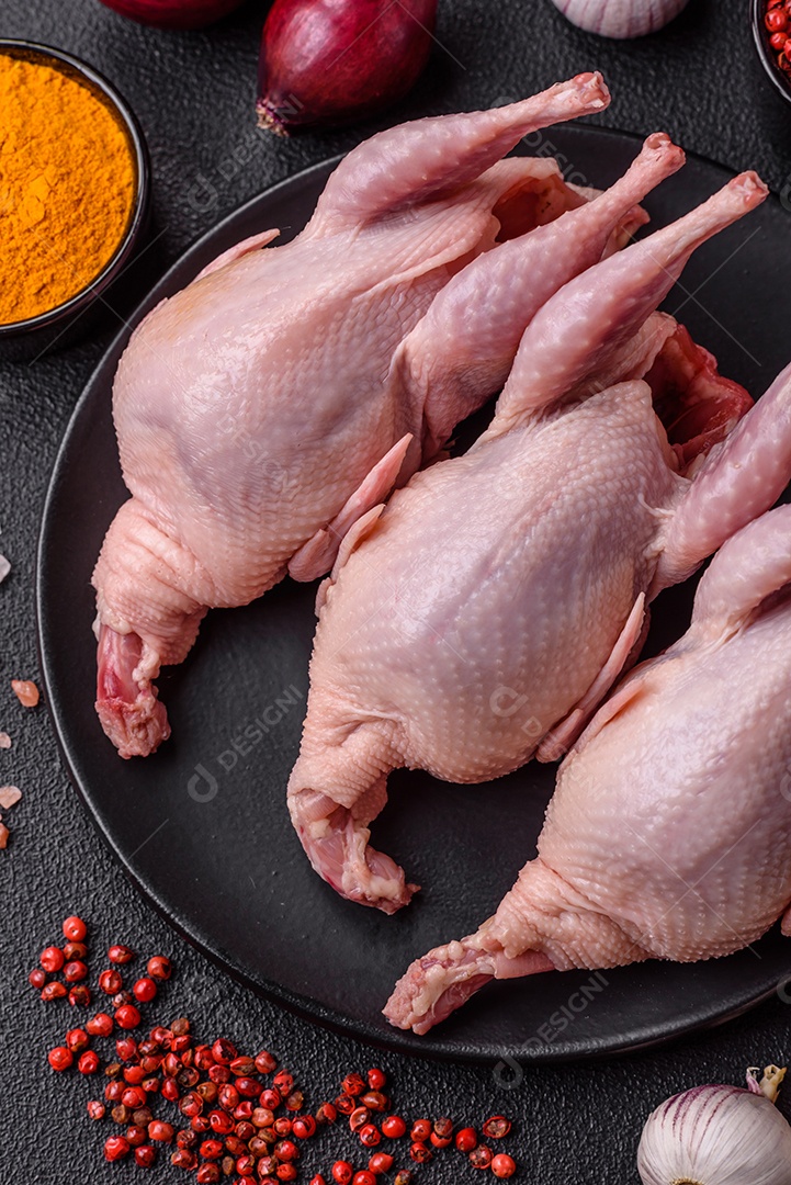 Codornizes cruas inteiras com sal, especiarias e ervas sobre um fundo escuro de concreto preparado para assar