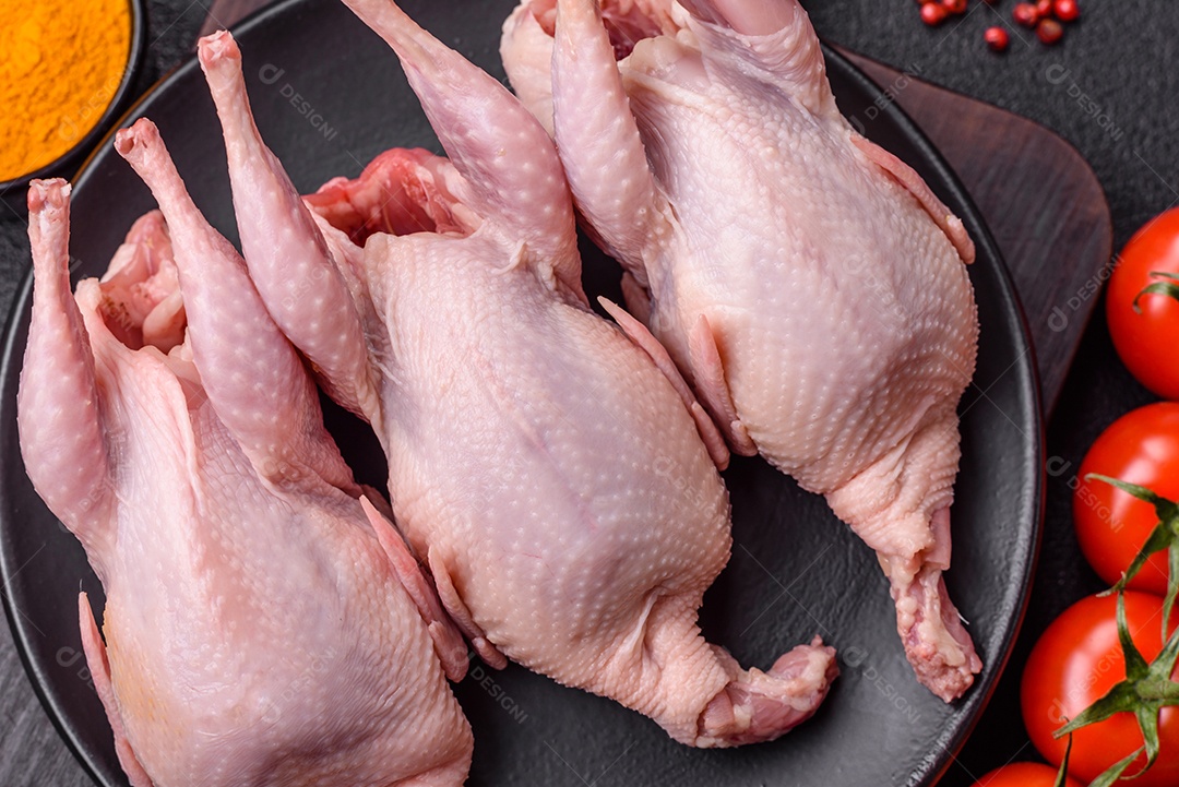 Codornizes cruas inteiras com sal, especiarias e ervas sobre um fundo escuro de concreto preparado para assar