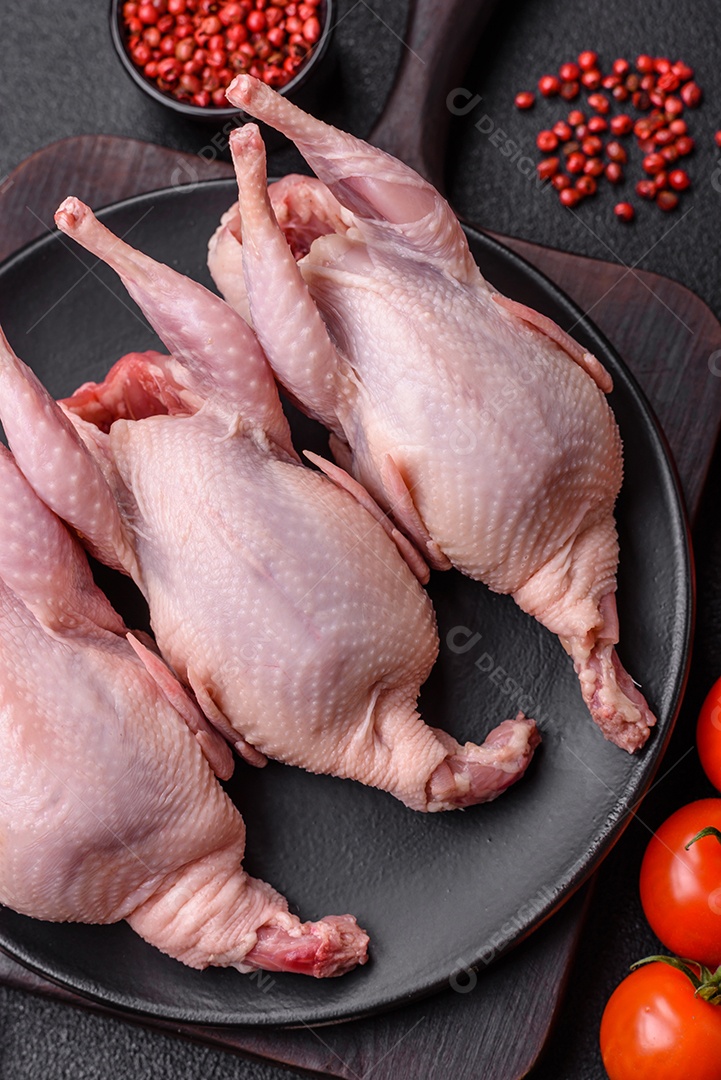 Codornizes cruas inteiras com sal, especiarias e ervas sobre um fundo escuro de concreto preparado para assar