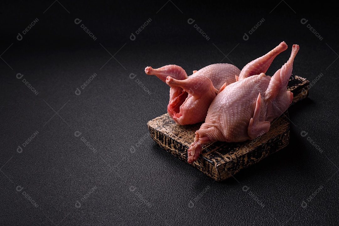 Codornizes cruas inteiras com sal, especiarias e ervas sobre um fundo escuro de concreto preparado para assar