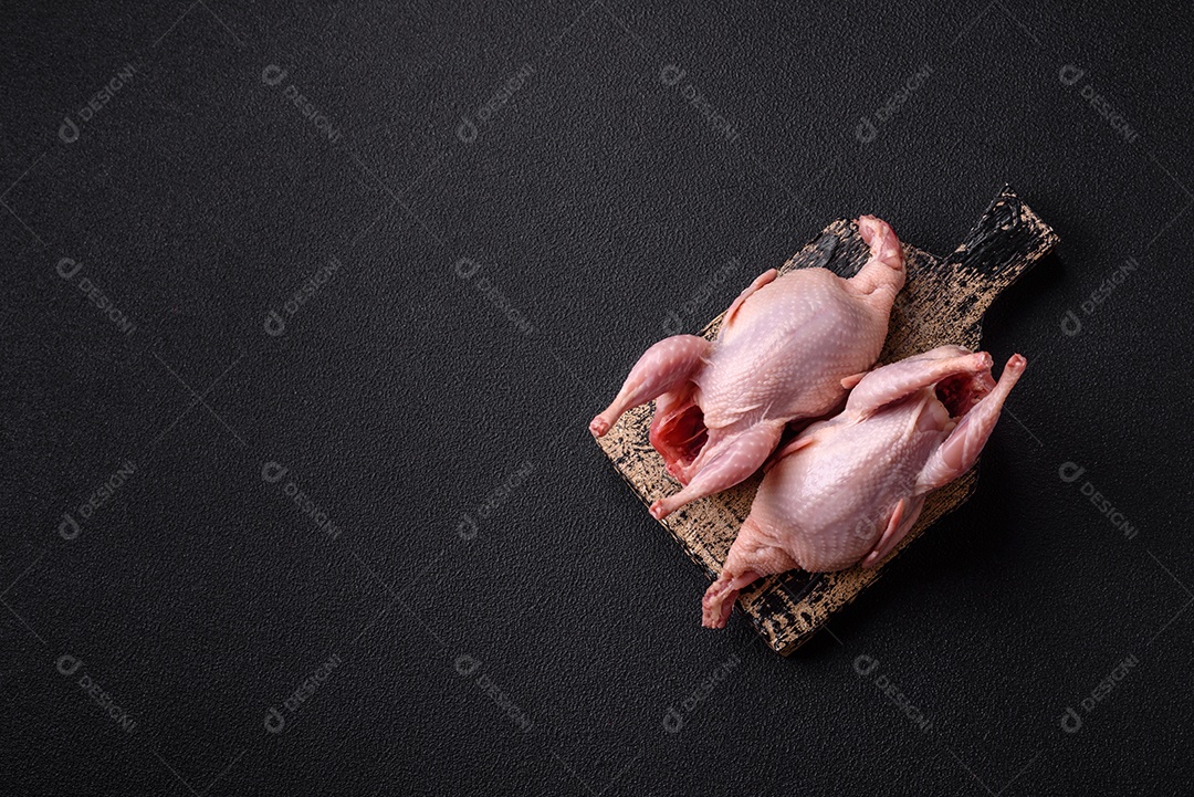 Codornizes cruas inteiras com sal, especiarias e ervas sobre um fundo escuro de concreto preparado para assar