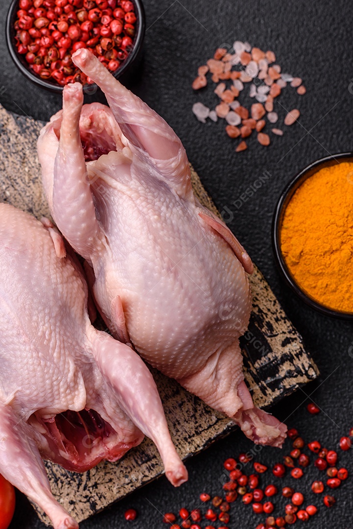 Pernas de frango cru com sal, especiarias e ervas sobre um fundo escuro de concreto preparado para assar