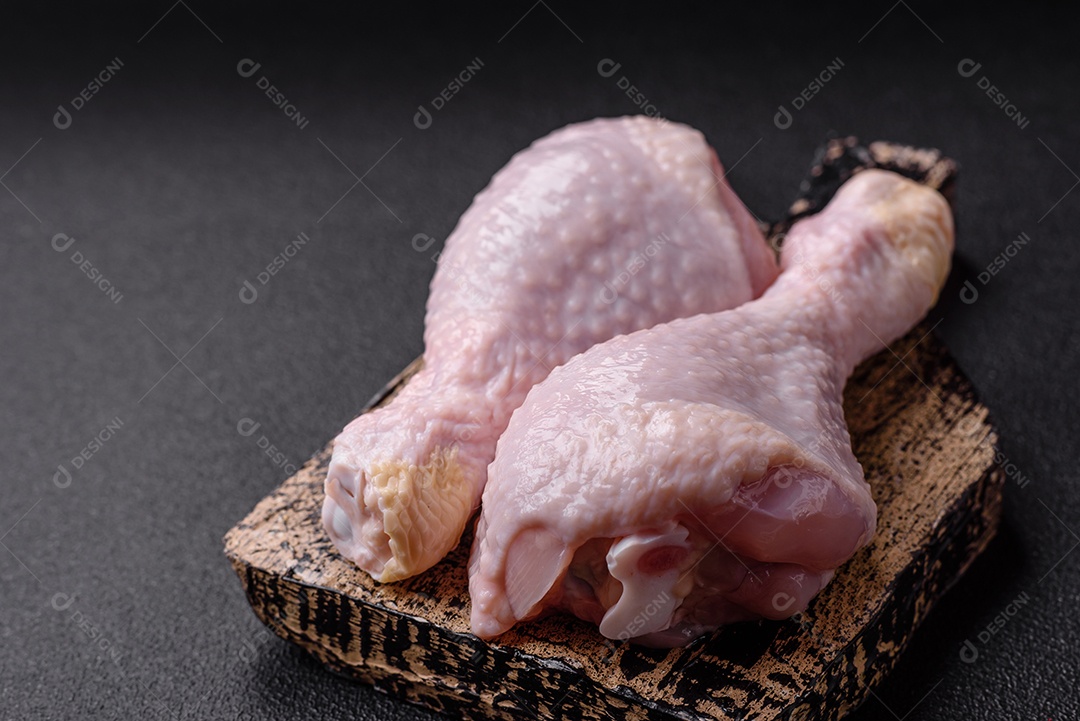 Pernas de frango cru com sal, especiarias e ervas sobre um fundo escuro de concreto preparado para assar