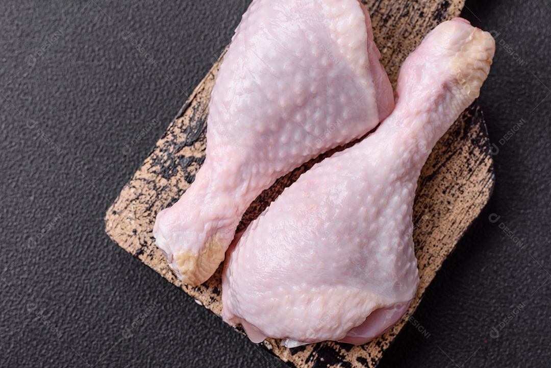 Pernas de frango cru com sal, especiarias e ervas sobre um fundo escuro de concreto preparado para assar