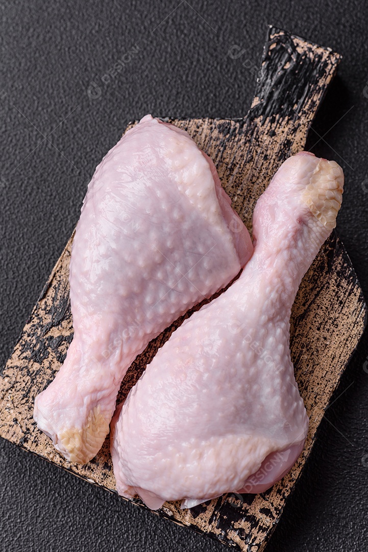 Pernas de frango cru com sal, especiarias e ervas sobre um fundo escuro de concreto preparado para assar