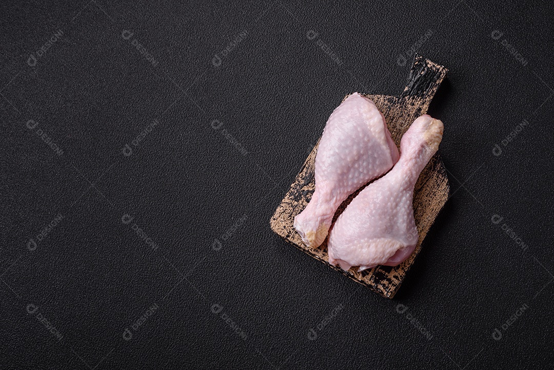 Pernas de frango cru com sal, especiarias e ervas sobre um fundo escuro de concreto preparado para assar