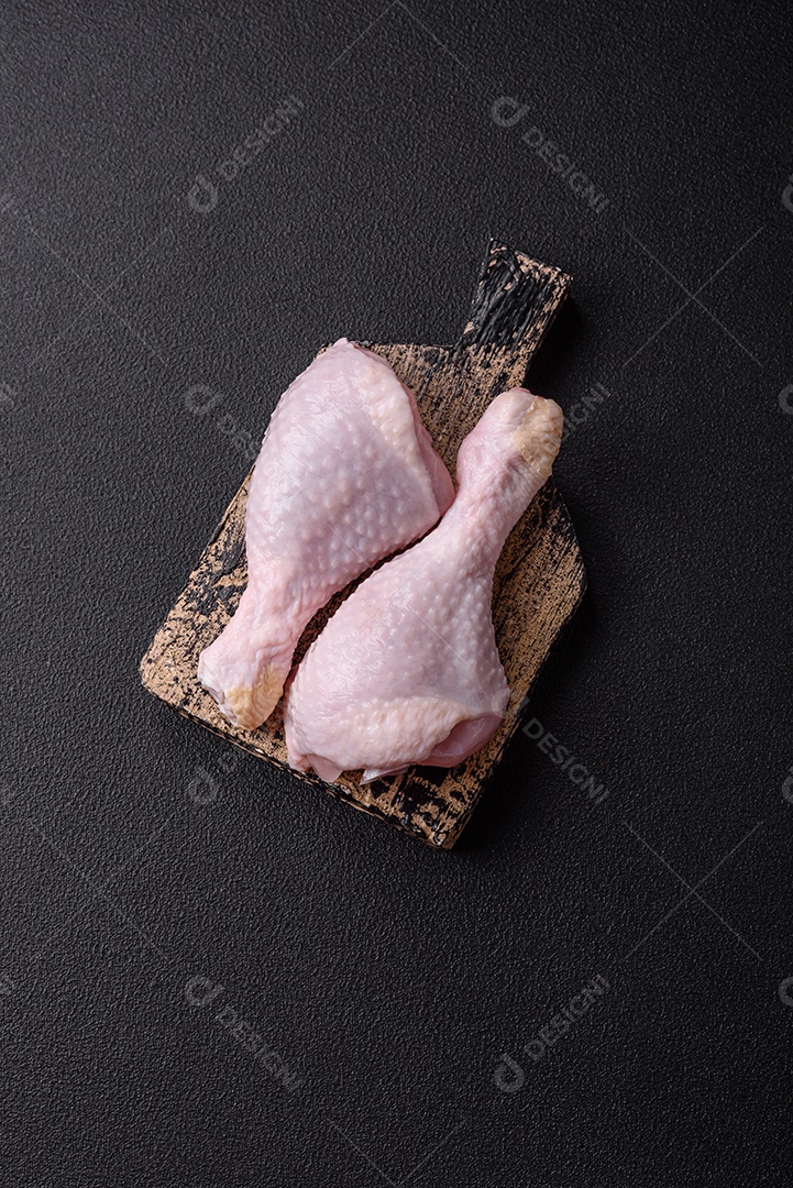 Pernas de frango cru com sal, especiarias e ervas sobre um fundo escuro de concreto preparado para assar