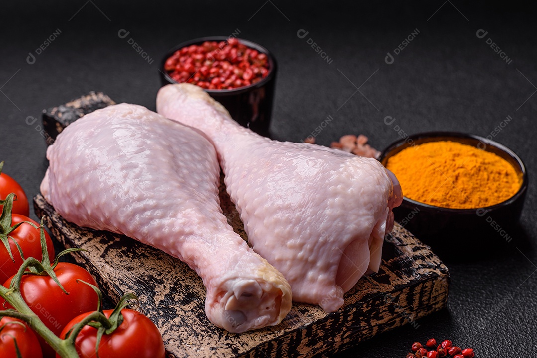 Pernas de frango cru com sal, especiarias e ervas sobre um fundo escuro de concreto preparado para assar