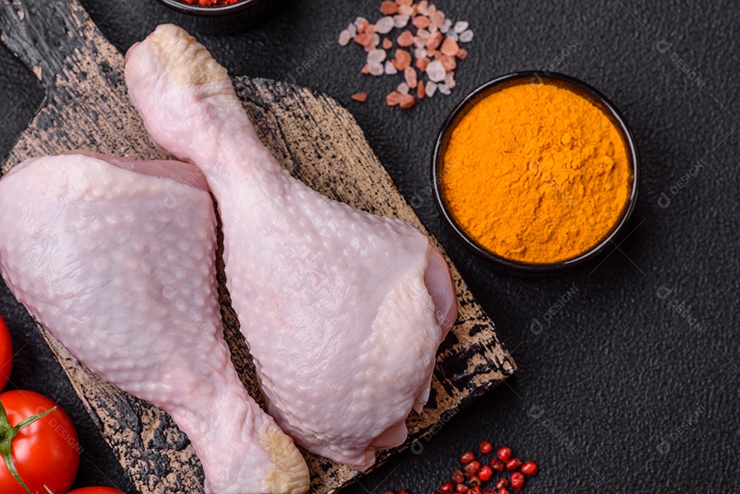 Pernas de frango cru com sal, especiarias e ervas sobre um fundo escuro de concreto preparado para assar