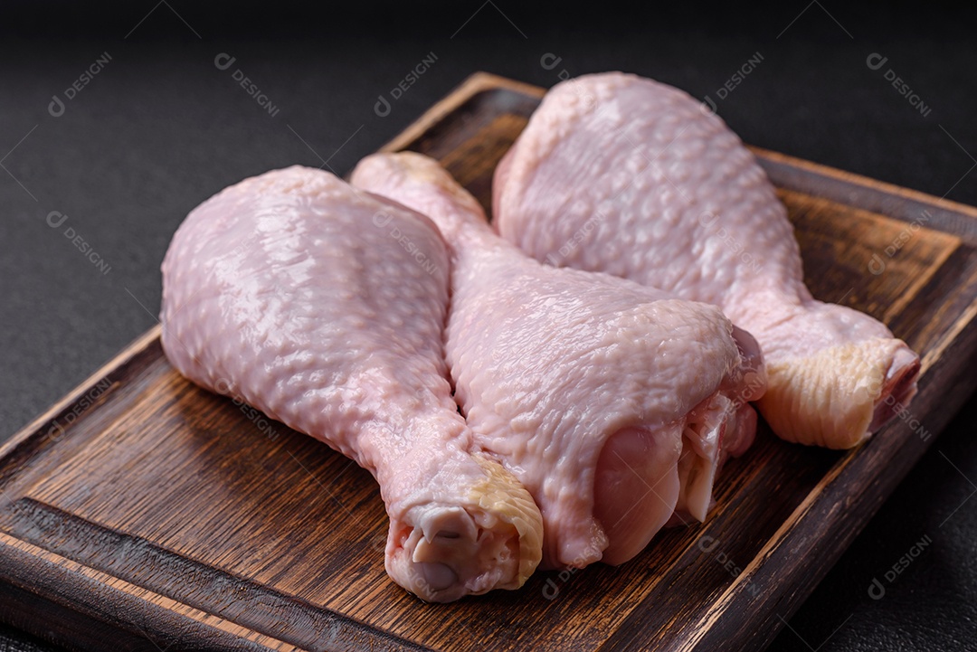 Pernas de frango cru com sal, especiarias e ervas sobre um fundo escuro de concreto preparado para assa
