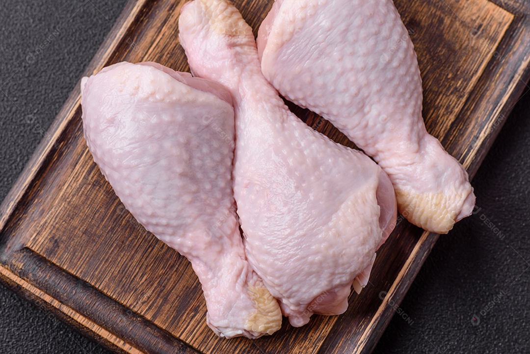 Pernas de frango cru com sal, especiarias e ervas sobre um fundo escuro de concreto preparado para assar