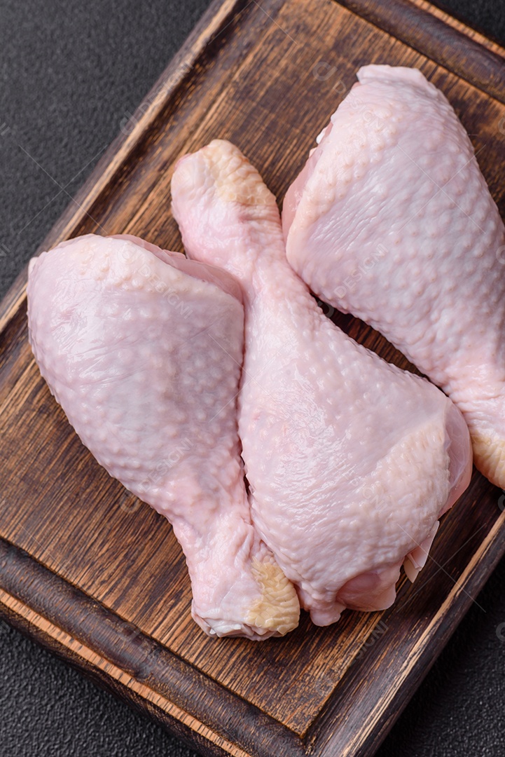 Pernas de frango cru com sal, especiarias e ervas sobre um fundo escuro de concreto preparado para assar