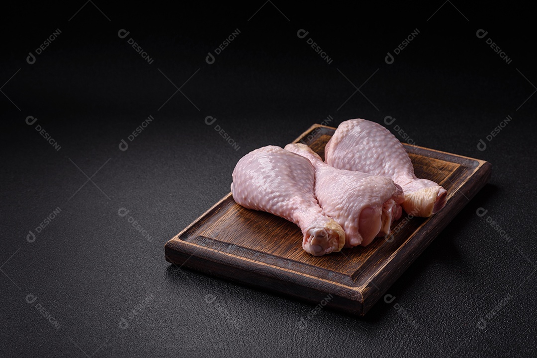 Pernas de frango cru com sal, especiarias e ervas sobre um fundo escuro de concreto preparado para assar